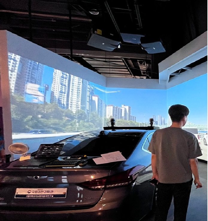 Autonomous-driving experience space with city driving video projected on the wall in front of a real vehicle